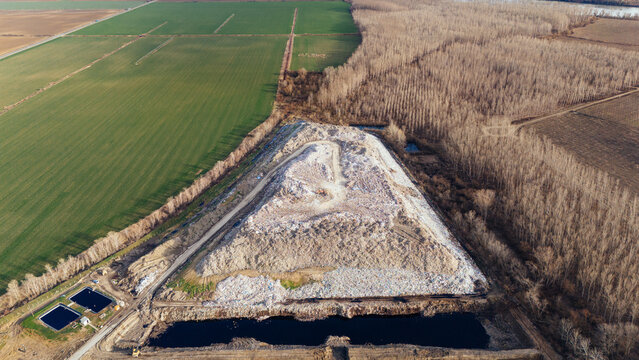Aerial view of a landfill with stark contrast of white waste against dark pools and adjacent green fields, Sremska Mitrovica, Vojvodina, Serbia.