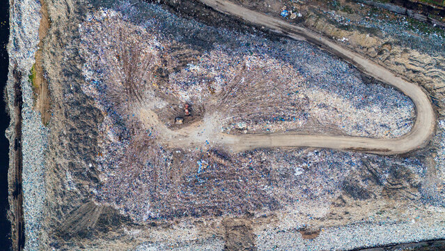 Aerial view of a vast landfill marked by a winding dirt road cutting through the piles of waste, a stark landscape of environmental concern, Sremska Mitrovica, Vojvodina, Serbia.