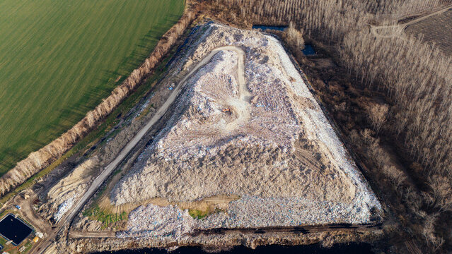 Aerial view of a vast landfill contrasting sharply with the surrounding lush green fields and dense woodland, showcasing environmental impact, Sremska Mitrovica, Vojvodina, Serbia.