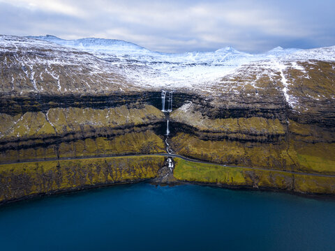 Aerial view of the cascading Fossa waterfall plunging powerfully down the cliffside into the deep blue waters below, Fossa, Vagar, Faroe Islands.