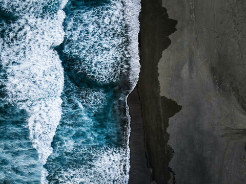 Aerial view of the dark sandy beach kissed by the frothy turquoise waves, creating a mesmerizing contrast of textures and tones, Santa Barbara, Azores, Portugal.