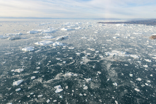Aerial view of scattered icebergs floating on the dark, frigid waters near the rugged, distant coastline, Ilulissat, Greenland.