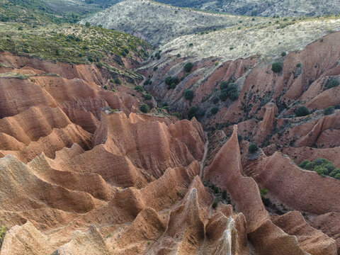 Aerial view of the vibrant red canyons contrasting with the sparse greenery, creating a dramatic landscape of erosion, Valdepenas de la Sierra, Castile-La Mancha, Spain.