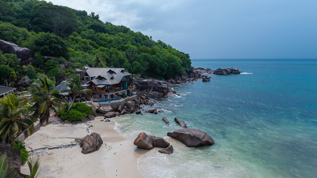 Aerial view of a luxury villa nestled among granite boulders and lush greenery, where the turquoise ocean meets the pristine white sands, Takamaka, Mahe, Seychelles.