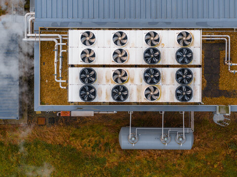 Aerial view of a rooftop HVAC system releasing steam, the metallic structure contrasting with the surrounding grassy expanse, Tredarzec, Bretagne, France.