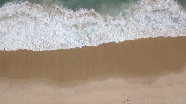Aerial view of foamy waves crash onto the golden sands of the shore, creating a mesmerizing dance of textures and tones, Rio de Janeiro, State of Rio de Janeiro, Brazil.