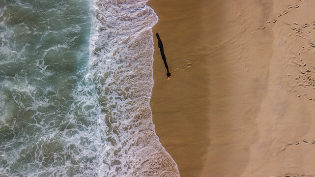 Aerial view of foamy waves caressing the golden sands where a solitary figure casts a long shadow, Rio de Janeiro, State of Rio de Janeiro, Brazil.