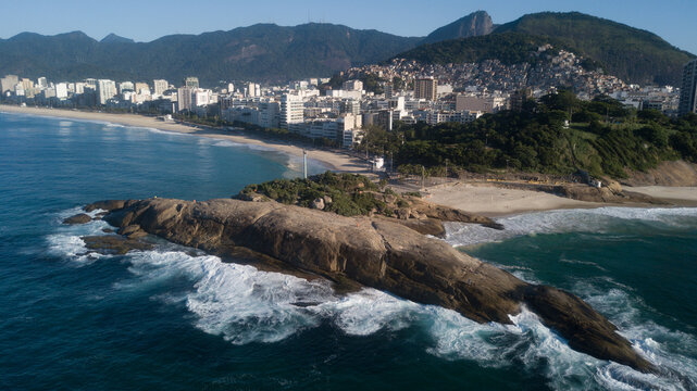 Aerial view of waves crash against the rocky outcrop contrasting with the city skyline and mountains, Rio de Janeiro, State of Rio de Janeiro, Brazil.