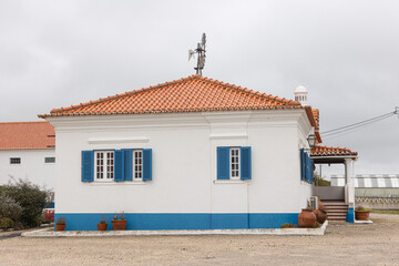 Obraz premium Traditional Portuguese house with white walls, blue shutters and terracotta tiled roof under cloudy sky.