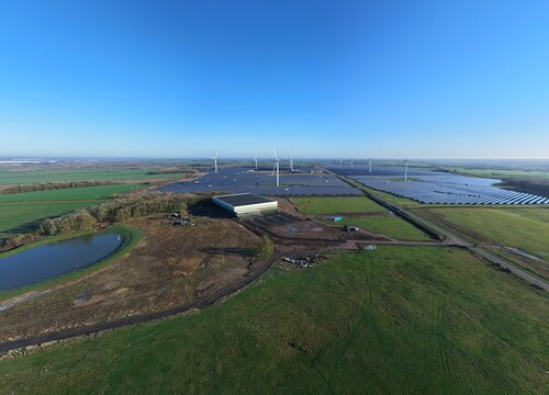 Aerial view of a landscape where turbines stand tall amidst solar panels, reflecting the vast sky above, Chelverston, Wellingborough, United Kingdom.