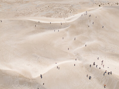 Aerial view of sun-drenched sand dunes dotted with tiny figures, creating a mesmerizing contrast between the vast landscape and human presence, Lancelin, Western Australia, Australia.