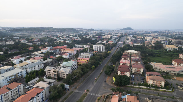 Aerial view of buildings stand amidst verdant trees, as roads bisect the landscape towards distant hills, Abuja, Federal Capital Territory, Nigeria.