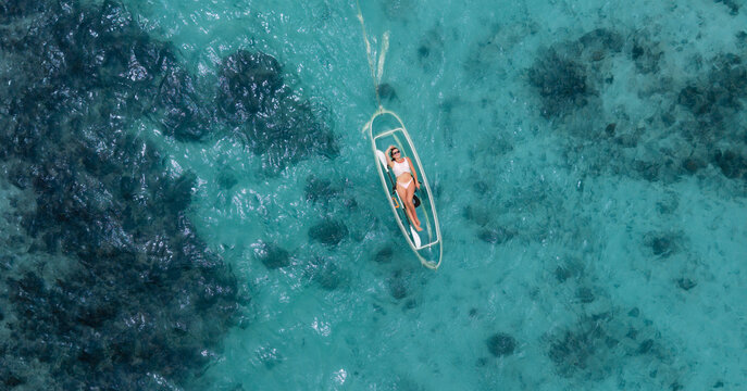 Aerial view of a woman lounging in a transparent kayak, the sun glinting off the turquoise water, Anse Reunion, La Digue, Seychelles.