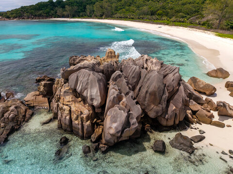 Aerial view of turquoise waters gently lap against the pale sands, contrasting with the dark, sculpted granite formations, Anse Reunion, La Digue, Seychelles.