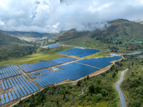 Aerial view of solar panels gleam under the diffused sunlight, nestled amidst rolling hills and shrouded in mist, Chemaito, Bhutan.