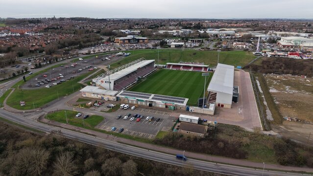 Northampton, United Kingdom - 14 February 2026: Aerial view of Northampton Town Football Club's stadium, a tapestry of green pitch and red seating, framed by grey skies and surrounding cityscape.