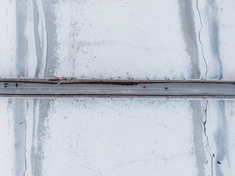 Aerial view of a bridge cutting through the stark white expanse of ice, a ribbon of grey against the frosted landscape, Vilnius, Lithuania.