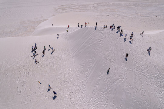 Aerial view of people scattered across the undulating, pristine white sand dunes under a stark, cloudless sky, Lancelin, Western Australia, Australia.