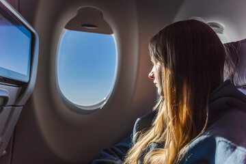 Fototapeta premium Young woman passenger looking through airplane window during flight