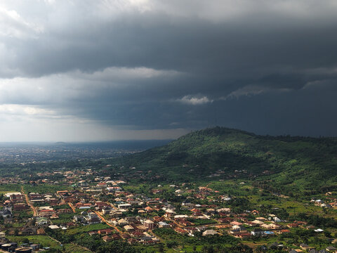 Aerial view of the town nestled amidst rolling green hills, a dramatic contrast of light and shadow under a brooding sky, Ilesa, Osun, Nigeria.