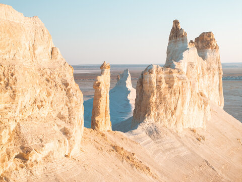 Aerial view of colossal chalk cliffs bathed in the golden sunlight, casting stark shadows across the desolate landscape, Aktau, Mangystau Region, Kazakhstan.