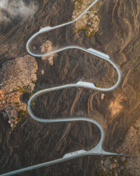 Aerial view of a winding road snaking through the volcanic landscape, a ribbon of pale grey against the dark earth, Nicolosi, Sicily, Italy.