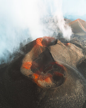 Aerial view of the volcanic landscape, where the stark black earth meets the fiery orange craters, as steam gracefully ascends into the vast sky, Nicolosi, Sicily, Italy.