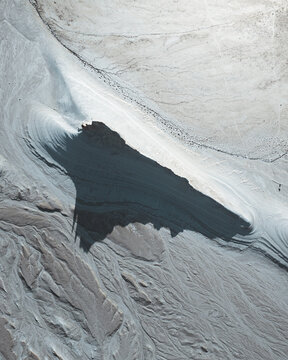Aerial view of a dark, irregular pool nestled within the arid, textured landscape, creating a stark contrast of color and form, Aktau, Mangystau Region, Kazakhstan.