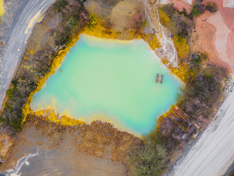 Aerial view of a serene turquoise lake nestled amidst the rugged, rust-colored earth, a stark contrast of nature's hues, Plouasne, Brittany, France.