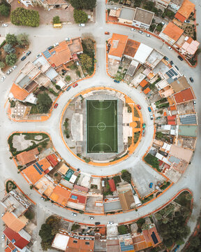 Aerial view of a vibrant football field nestled in a circular arrangement of terracotta-roofed buildings, creating a captivating geometric pattern, Naples, Campania, Italy.