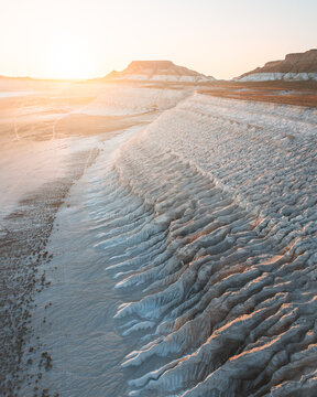 Aerial view of the stunning, sun-kissed cliffs and rugged terrain casting long shadows across the vast, arid landscape, Mangystau Region, Kazakhstan.
