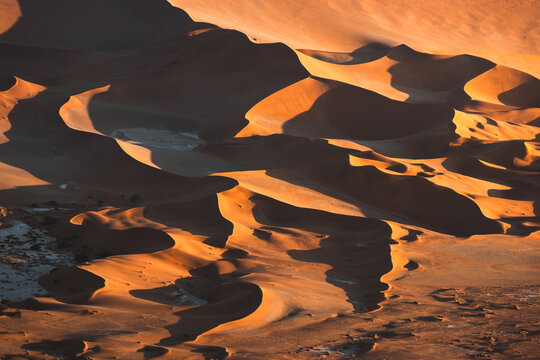 Aerial view of the undulating dunes cast dramatic shadows in the Namib desert, creating a mesmerizing landscape of golden hues, Sossusvlei, Hardap Region, Namibia.