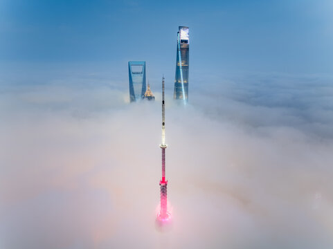 Aerial view of skyscrapers piercing through a sea of swirling fog, with the Oriental Pearl Tower's vibrant pink and red lights reflecting in the mist, Pu Dong Xin Qu, Shang Hai Shi, China.