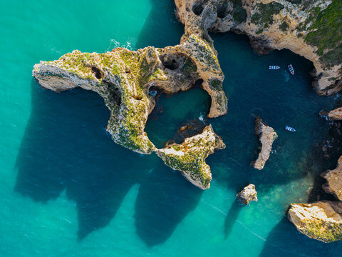 Aerial view of dramatic cliffs of Ponta da Piedade meeting the turquoise sea, a symphony of blues and greens, sculpted by time and tide, Lagos, Faro, Portugal.