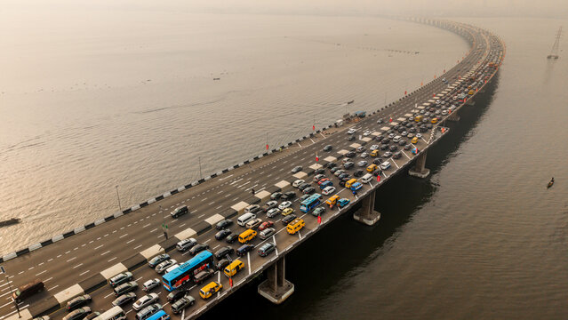 Aerial view of dense traffic flowing across the Third Mainland Bridge, a ribbon of concrete cutting through the shimmering water, Lagos, Lagos, Nigeria.