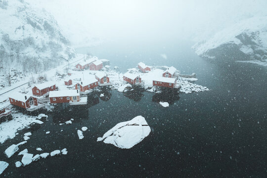 Aerial view of red cabins contrast against the dark water and snowy landscape, Nusfjord, Nordland, Norway.