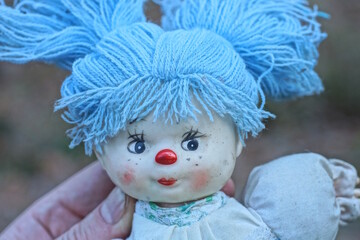 hand holding one toy doll with blue hair on summer street