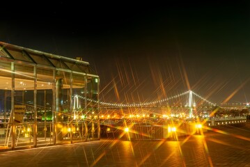 Fototapeta premium 竹芝客船ターミナル・ボードウォークの夜景：光り輝くレインボーブリッジと都会の海辺 / Night View from Takeshiba Passenger Ship Terminal Boardwalk: Sparkling Rainbow Bridge and Urban Waterfront