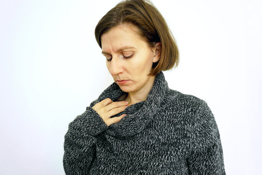 Woman in sweater touches her neck with half-closed eyes. Depicts throat pain, thyroid discomfort, or seasonal fatigue, suitable for health content about winter illness and chronic somatic symptoms.