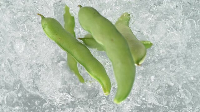 Broad Bean Pods Falling Into Pot Of Boiling Water Making A Splash In Slow Motion, Table Top View