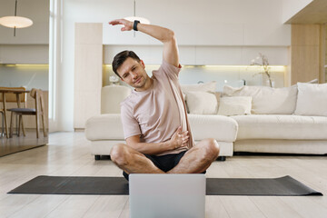 Man stretches at home while following an online exercise session in the morning
