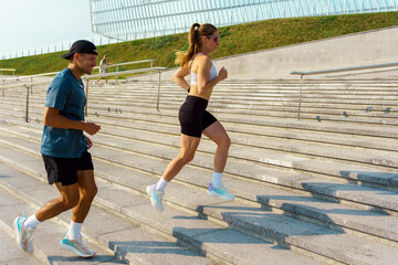 Two people run up steps in a public area during daytime in a city setting while enjoying their exercise routine together