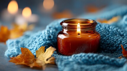A cozy scene with a lit candle, blue knit fabric, golden leaves, and blurred bokeh lights
