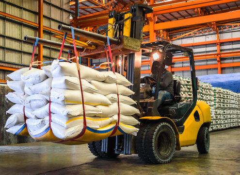 Forklift handling large white jumbo bags of refined sugar in an industrial warehouse for logistics and export.
