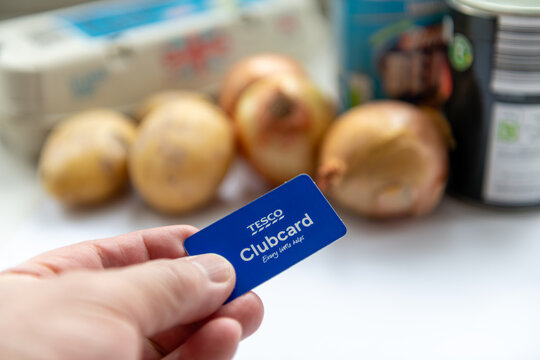 London. UK- February 15. 2026. A person holding a Tesco Clubcard with various grocery items in the background.