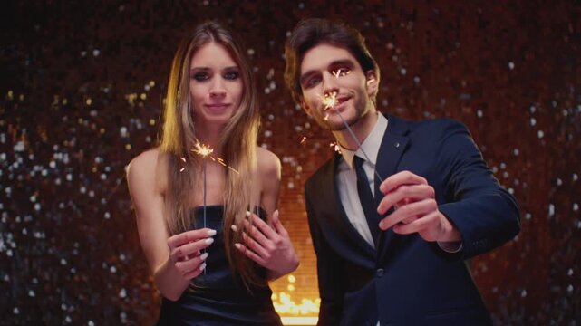 Happy couple with sparklers at party. Celebration, fun and holidays. Man and woman with Bengali fire or fire stick glow. Male, female celebrate New Year or Christmas, xmas together. Burning sparkle