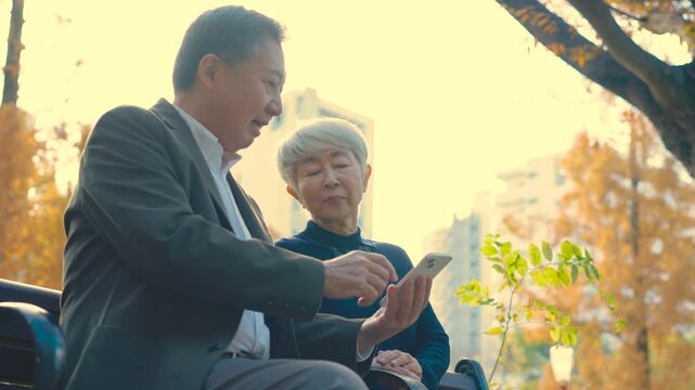 ベンチに座ってスマホを見るシニア男女