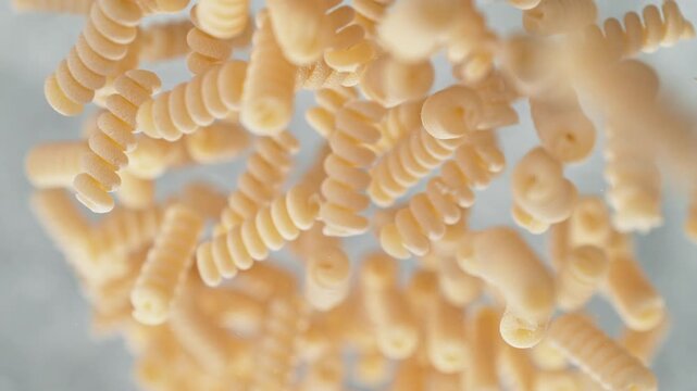 Spiralini Pasta Falling Into Pot Of Boiling Water Making A Splash In Slow Motion, Table Top View