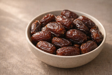 Obraz premium A bowl of dates placed on a textured brown surface, captured from a slightly elevated viewpoint