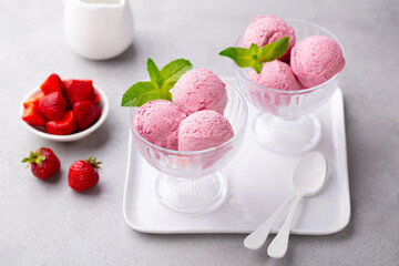 Strawberry ice cream served in elegant glass dishes, with a side of sliced strawberries and mint leaves. Grey background. Close up. © annapustynnikova